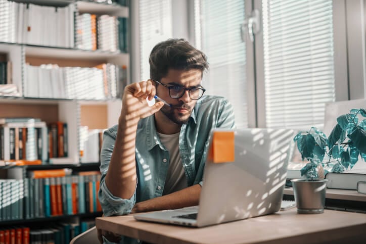 student staring at computer with pen in hand