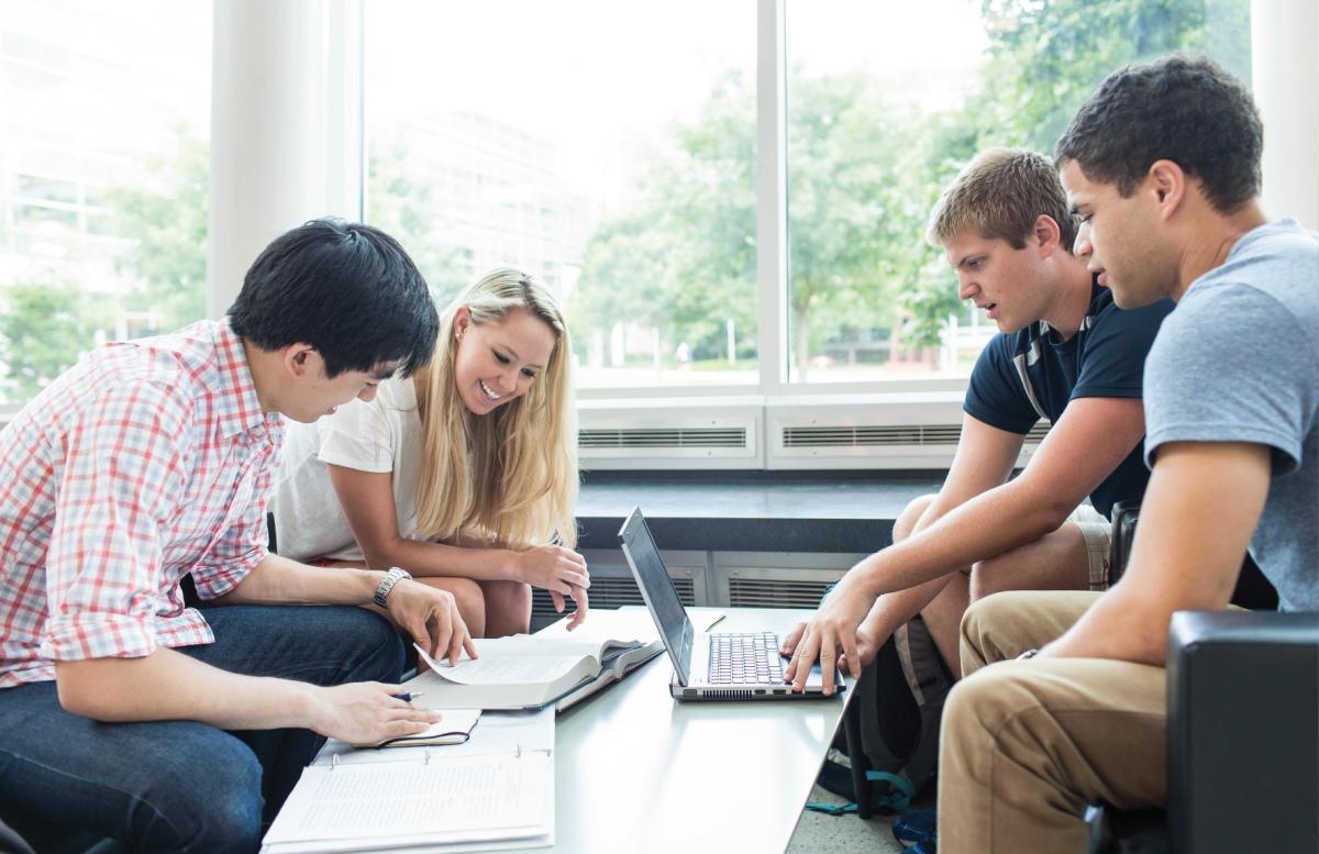 students sitting in the grass reviewing books